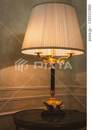 Old fashioned lamp with lampshade on a table. Hotel room design. Cozy home style. Classic home design. Bedroom lamp on table in the evening. Night light equipment. Elegant interior design. Old fashioned lamp with lampshade on a table. Hotel room design. Cozy home style. Classic home design. Bedroom lamp on table in the evening. Night light equipment. Elegant interior design. 139331966