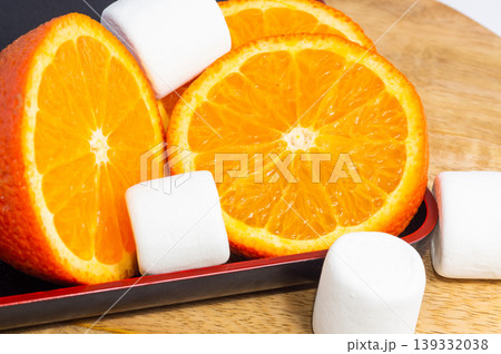 A sliced orange and white marshmallows lie on a wooden board. A sliced orange and white marshmallows lie on a wooden board. 139332038