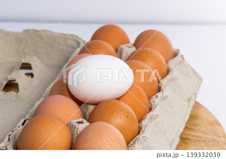 A white egg rests on top of the package of brown eggs. A white egg rests on top of the package of brown eggs. 139332039