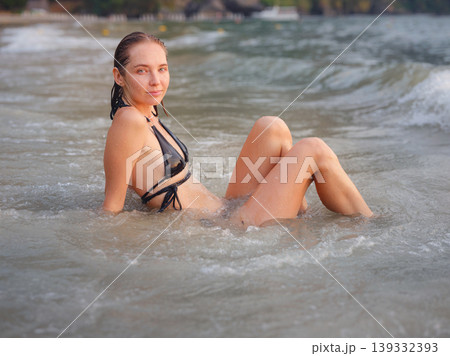 Young woman enjoying serene evening at sea in Krabi, Thailand during sunset. Calm waves, golden light, and peaceful atmosphere highlight tropical beauty and connection with nature. Young woman enjoying serene evening at sea in Krabi, Thailand during sunset. Calm waves, golden light, and peaceful atmosphere highlight tropical beauty and connection with nature. 139332393