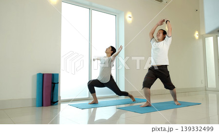 Man and woman practicing warrior yoga variation with arm extension at home, improving strength, balance and flexibility, enhancing full body coordination in bright minimalist indoor fitness space 139332499