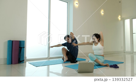Man and woman practicing seated spinal twist yoga pose at home, improving flexibility, enhancing spine mobility and posture, relieving tension and promoting wellness in bright minimalist indoor 139332527