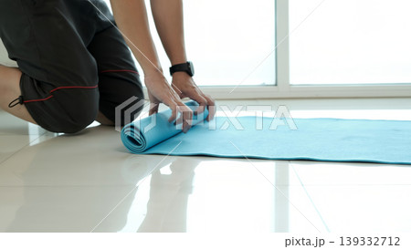 Close-up of person rolling yoga mat on floor at home, preparing for fitness workout and wellness routine, highlighting healthy lifestyle, exercise setup, indoor activity and minimal space training Close-up of person rolling yoga mat on floor at home, preparing for fitness workout and wellness routine, highlighting healthy lifestyle, exercise setup, indoor activity and minimal space training 139332712