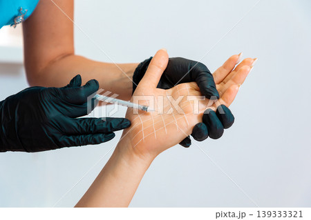 Cosmetologist makes injections of botulinum toxin on the female palm against hyperhidrosis. Hand with white drawn grid. Close up. Concept of cosmetology Cosmetologist makes injections of botulinum toxin on the female palm against hyperhidrosis. Hand with white drawn grid. Close up. Concept of cosmetology 139333321
