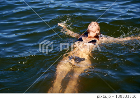Bikini, woman and floating in water at lake to relax in summer, holiday and swimming on vacation. Calm, peace and person in swimwear, fashion or body in waves of ocean or sea with freedom in nature Bikini, woman and floating in water at lake to relax in summer, holiday and swimming on vacation. Calm, peace and person in swimwear, fashion or body in waves of ocean or sea with freedom in nature 139333510