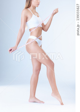 Woman, measuring tape and waist in studio with underwear, thinking and check for progress by white background. Girl, model and person with body inspection for health, weight loss or stomach growth 139333827