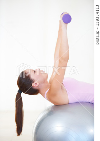 Woman, lying and exercise on ball, dumbbells and balance in gym, training and strong muscle in arms. Girl, profile and fitness with workout, weightlifting and hard work for health, wellness and body Woman, lying and exercise on ball, dumbbells and balance in gym, training and strong muscle in arms. Girl, profile and fitness with workout, weightlifting and hard work for health, wellness and body 139334113