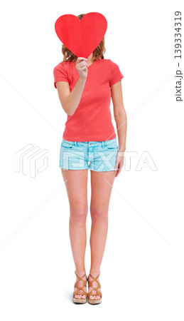 Woman, heart and studio for valentines secret or poster mockup, emoji icon or white background. Female person, hiding face and cardboard love symbol for shy date admirer, romance gift or news space 139334319