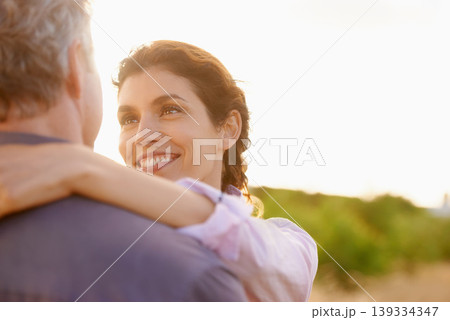 Mature, couple and smile in embrace at sunset with love, trust and support in marriage or partnership. Happy, woman and care together with freedom, health or wellness at beach for vacation or holiday 139334347