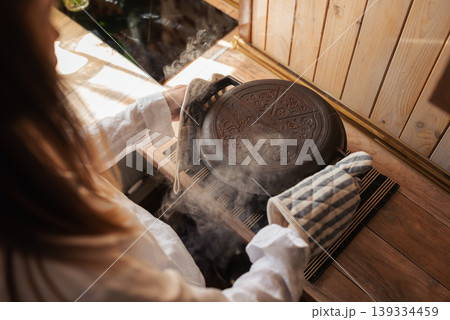 Girl hostess taking hot pot from the oven with baked bread. Hot pot with steam around, baking at home concept 139334459