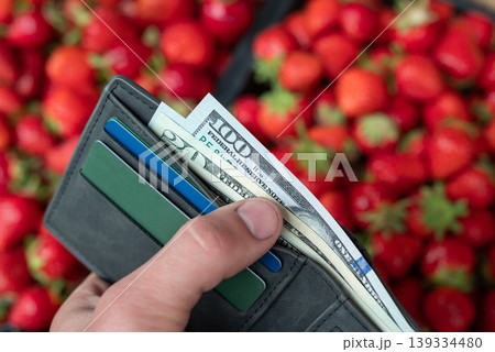 Looking through money in wallet with strawberry background at the market. Concept of buying expensive but tasty strawberry Looking through money in wallet with strawberry background at the market. Concept of buying expensive but tasty strawberry 139334480