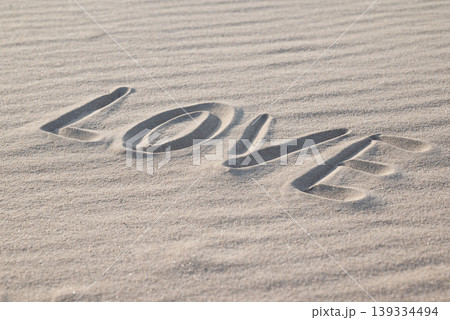 Side view on a word "love" written on the wavy sand, close up. Concept of being in love, passionate feelings, falling in love Side view on a word "love" written on the wavy sand, close up. Concept of being in love, passionate feelings, falling in love 139334494