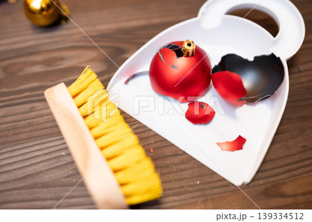 Broken christmas tree decoration in white scoop. Cleaning floor from broken decoration with brush and scoop Broken christmas tree decoration in white scoop. Cleaning floor from broken decoration with brush and scoop 139334512