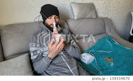 Vertical portrait of an adult man breathing through a clinical nebulizer, domestic respiratory therapy, wellness recovery session, medicine Vertical portrait of an adult man breathing through a clinical nebulizer, domestic respiratory therapy, wellness recovery session, medicine 139334670