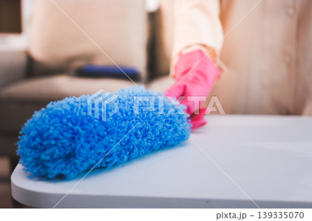 Person cleaning the room, cleaning staff is using cloth and spraying disinfectant to wipe the tables in the company office room. Cleaning staff. Maintaining cleanliness in the organization. 139335070