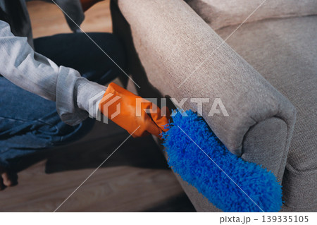 Person cleaning the room, cleaning staff is using cloth and spraying disinfectant to wipe the tables in the company office room. Cleaning staff. Maintaining cleanliness in the organization. 139335105