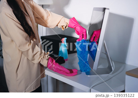 Person cleaning the room, cleaning staff is using cloth and spraying disinfectant to wipe the tables in the company office room. Cleaning staff. Maintaining cleanliness in the organization. 139335122