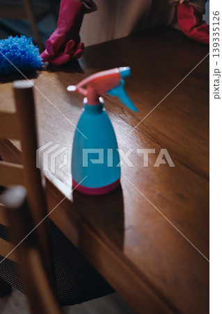 Person cleaning the room, cleaning staff is using cloth and spraying disinfectant to wipe the tables in the company office room. Cleaning staff. Maintaining cleanliness in the organization. 139335126