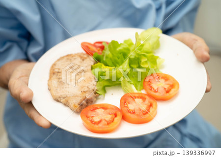 Asian elderly woman patient eating pork chop stake and vegetable salad for healthy food in hospital. 139336997