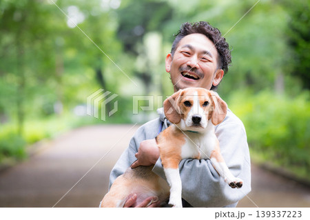 新緑背景で愛犬のビーグルを抱く男性の笑顔、公園で過ごす幸せなお散歩時間のカメラ目線クローズアップ 139337223