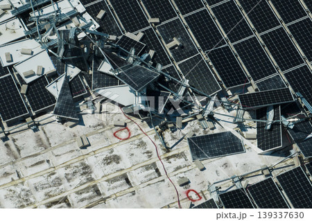 Aerial view of damaged by hurricane wind photovoltaic solar panels mounted on industrial building roof for producing green ecological electricity. Consequences of natural disaster 139337630