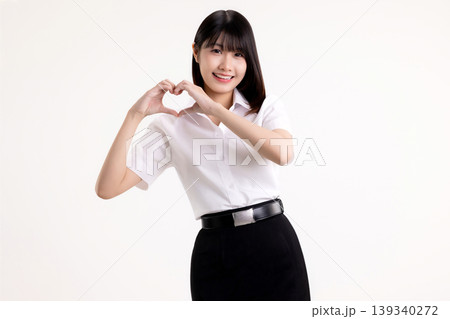 Lovely young Asian woman in white shirt student uniform making heart shape with hands. Happy female university student smiling and looking at camera, showing love and care symbol on white background. Lovely young Asian woman in white shirt student uniform making heart shape with hands. Happy female university student smiling and looking at camera, showing love and care symbol on white background. 139340272
