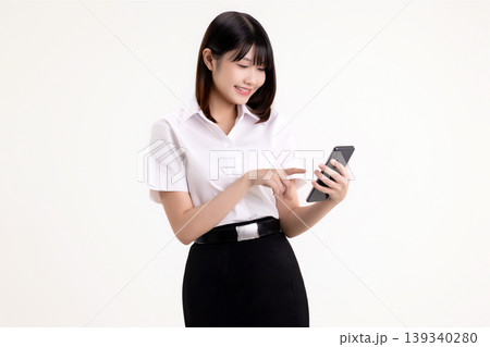 Happy young Asian woman in student uniform using smartphone and touching the screen. Smiling female university student holding mobile phone and browsing social media, isolated on white background. Happy young Asian woman in student uniform using smartphone and touching the screen. Smiling female university student holding mobile phone and browsing social media, isolated on white background. 139340280