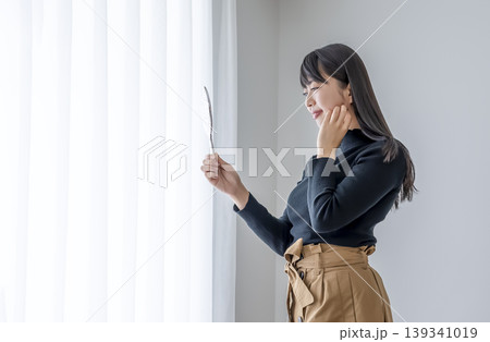 窓辺で肌の状態を確認する若い女性 窓辺で肌の状態を確認する若い女性 139341019