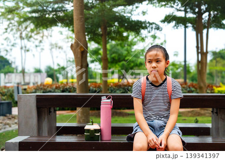 Cute Asian student girl with backpack sitting on a bench and waiting for the bus, Back to school concept. Cute Asian student girl with backpack sitting on a bench and waiting for the bus, Back to school concept. 139341397