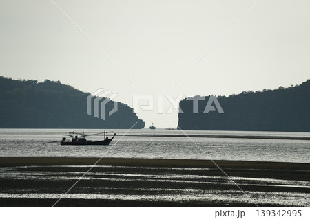 Silhouette of long-tail boat floating in the calm sea in front of the space between two islands 139342995