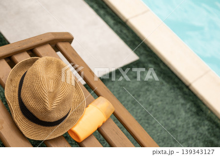 Poolside essentials: straw hat and sunscreen on a wooden lounge chair Poolside essentials: straw hat and sunscreen on a wooden lounge chair 139343127