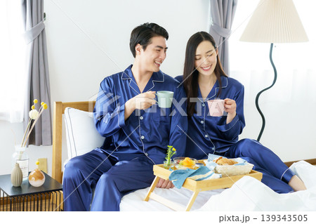 朝、ベッドの上で並んで微笑む若い日本人セレブカップル 139343505