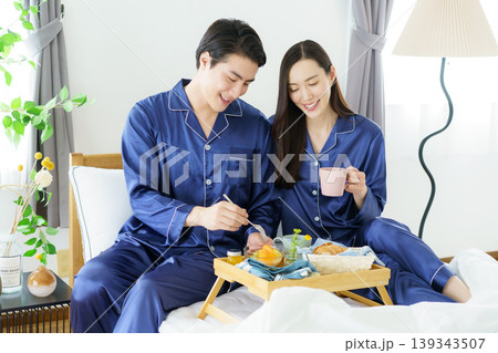 朝、ベッドの上で並んで朝食を食べようとする若い日本人セレブカップル 朝、ベッドの上で並んで朝食を食べようとする若い日本人セレブカップル 139343507