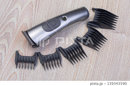 Electric hair clipper with various guard combs on wooden background Electric hair clipper with various guard combs on wooden background 139343590