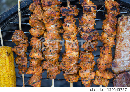 Close up of grilled chicken skewers with corn on barbecue grill, summer BBQ food cooking background Close up of grilled chicken skewers with corn on barbecue grill, summer BBQ food cooking background 139343727