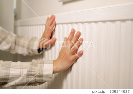 Woman warming up hands over heater. Increasing bills expenses. Cold season. Rising utility costs Woman warming up hands over heater. Increasing bills expenses. Cold season. Rising utility costs 139344027