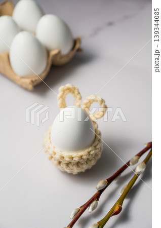 Easter background. White egg in a knitted bunny egg holder and pussy willow twigs. Spring time. Minimalistic Easter background. White egg in a knitted bunny egg holder and pussy willow twigs. Spring time. Minimalistic 139344085