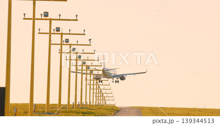 Passenger airplane approaching runway aligned with airport approach lighting system during golden hour. Perspective view of aviation infrastructure. Passenger airplane approaching runway aligned with airport approach lighting system during golden hour. Perspective view of aviation infrastructure. 139344513