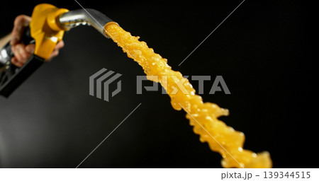 Gasoline jet spraying from fuel nozzle held by hand on dark background. Dynamic liquid motion, refueling concept, energy supply, fuel usage, dramatic lighting, macro detail. Gasoline jet spraying from fuel nozzle held by hand on dark background. Dynamic liquid motion, refueling concept, energy supply, fuel usage, dramatic lighting, macro detail. 139344515