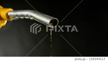 Gasoline drops dripping from fuel nozzle on dark background, minimal fuel flow. Concept of fuel depletion, shortage and energy crisis, macro detail, dramatic lighting. Gasoline drops dripping from fuel nozzle on dark background, minimal fuel flow. Concept of fuel depletion, shortage and energy crisis, macro detail, dramatic lighting. 139344517
