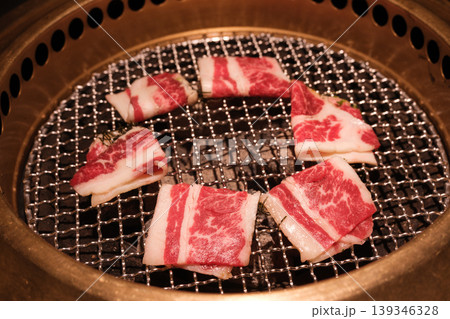 炭火焼肉グリルで焼かれる牛肉スライスとトングのクローズアップ 炭火焼肉グリルで焼かれる牛肉スライスとトングのクローズアップ 139346328