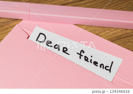 Pink envelope with a white note that reads dear friend on a wooden table with a pink pen Pink envelope with a white note that reads dear friend on a wooden table with a pink pen 139346838