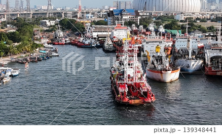 a red offshore supply and rescue ship equipped with a lattice tower, docked at a busy industrial port alongside various barges and heavy maritime equipment. 139348441