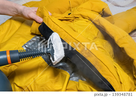 the process of steaming or cleaning a yellow down jacket using a steam cleaner 139348781