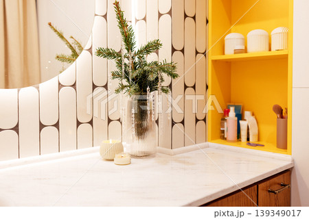Modern bathroom interior featuring a stylish countertop with a vase of greenery, candles, and beauty products, complemented by geometric patterned tiles and vibrant yellow accents 139349017