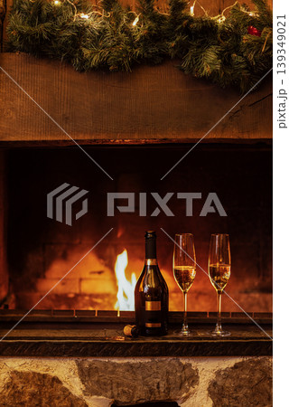 Close-up of two glasses of champagne on the fireplace. A bottle of sparkling wine and goblets near an open fire. The Christmas party or a romantic meeting. Close-up of two glasses of champagne on the fireplace. A bottle of sparkling wine and goblets near an open fire. The Christmas party or a romantic meeting. 139349021