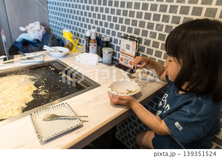 鉄板焼き店でもんじゃ焼きを食べる日本人の女の子の幼児 鉄板焼き店でもんじゃ焼きを食べる日本人の女の子の幼児 139351524