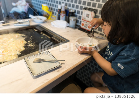 鉄板焼き店でもんじゃ焼きを食べる日本人の女の子の幼児 鉄板焼き店でもんじゃ焼きを食べる日本人の女の子の幼児 139351526