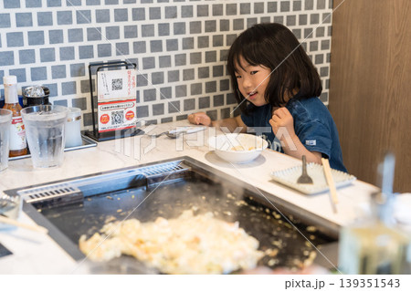 鉄板焼き店でもんじゃ焼きを食べる日本人の女の子の幼児 鉄板焼き店でもんじゃ焼きを食べる日本人の女の子の幼児 139351543