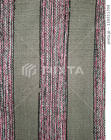 Traditional hand woven grey fabric featuring vertical stripes of black, white, and pink threads. It is often used in clothing and home decor items. 139351709